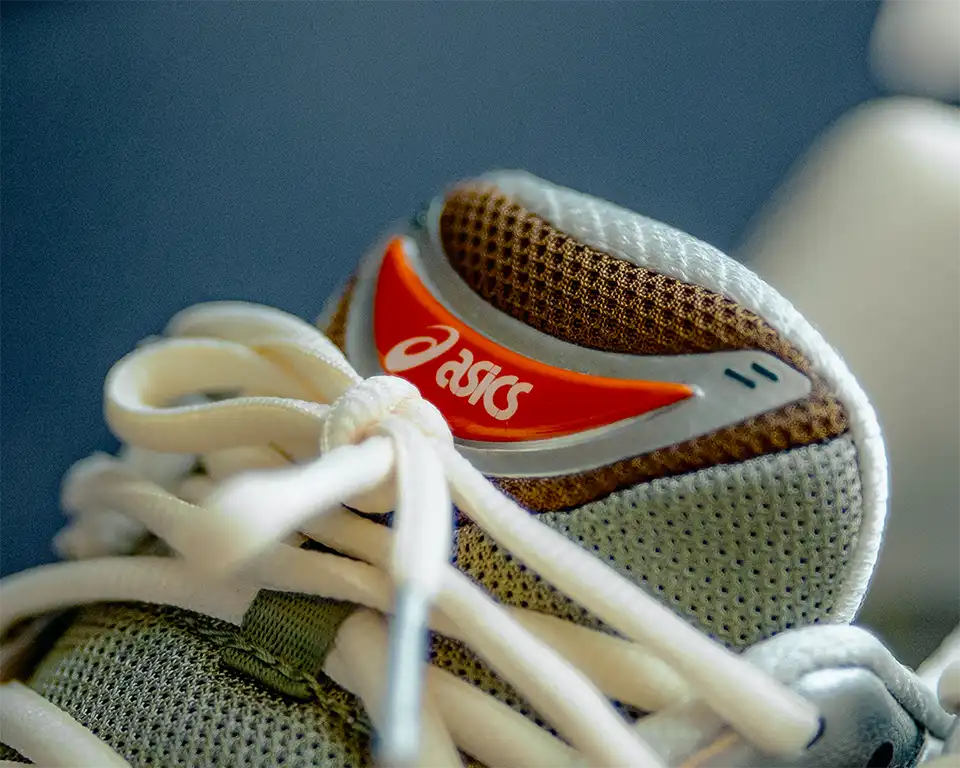 โลโก้ ASICS สีขาวบนพื้นสีส้ม บริเวณลิ้นรองเท้า